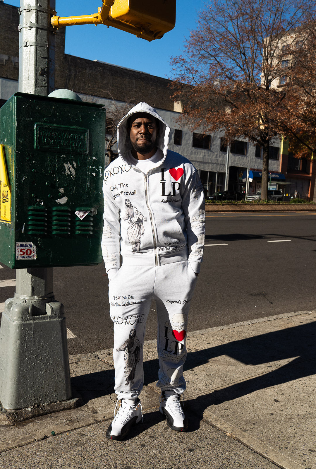 Person wearing a white hoodie and pants with text and graphics on a city street.